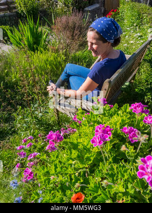 Woman Sitting on wooden bench in garden Stock Photo