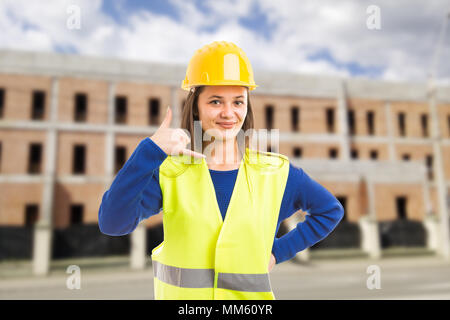 Young attractive female architect or engineer making call gesture as contact assistance person concept on construction building background Stock Photo