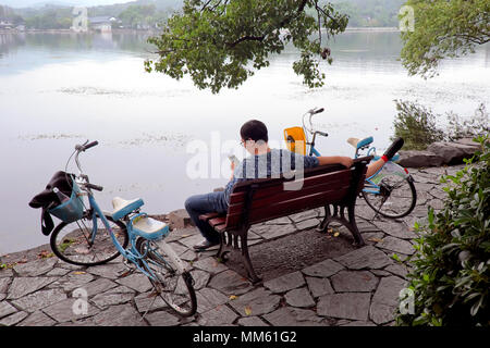 Man surfing / checking his mobile phone while his girlfriend takes a power nap, West Lake, Hangzhou, Zhejiang Province, China Stock Photo