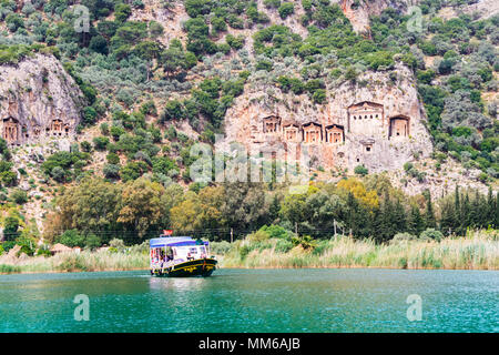 River boat with tourists on the river Dalyan by the sheer cliffs with the weathered facades of Lycian tombs cut from rock, circa 400 BC. Stock Photo