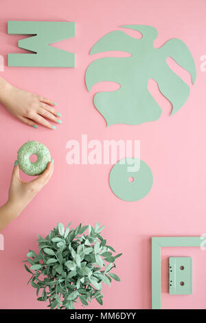 Mint color leaf, cd, plant and a woman holding a doughnut on a pink background Stock Photo
