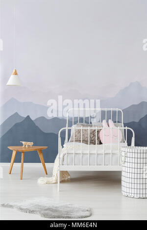 White metal frame bed by a wall with mountains wallpaper in a minimalist bedroom interior for a child with cute decorations and accessories Stock Photo