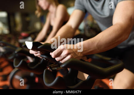Close-up of hands of a man biking in the gym, exercising legs doing cardio workout cycling bikes. Couple in a spinning class wearing sportswear. Stock Photo