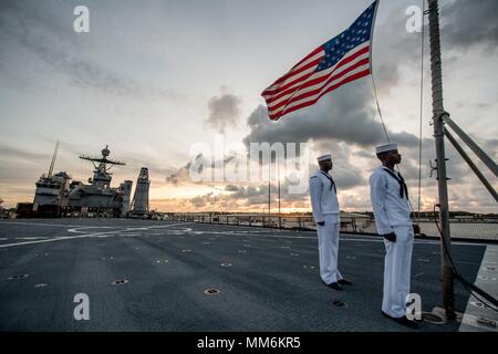 170911-N-UX013-776 NAVAL BASE GUAM (Sept. 11, 2017) Seaman Nayyaamunhotep Stubbs from West Palm Beach, Fla., left, and Hospitalman Kane Peters from St. Louis, post under the ensign, at half-mast, during first call to evening colors on the flight deck of the amphibious dock landing ship USS Ashland (LSD 48). Ashland flew the ensign at half-mast in honor of 9/11 victims during a scheduled port visit in Guam. (U.S. Navy photo by Mass Communication Specialist 3rd Class Jonathan Clay/Released) Stock Photo