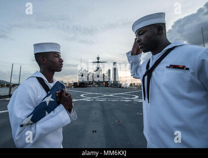 170911-N-UX013-822 NAVAL BASE GUAM (Sept. 11, 2017) Seaman Nayyaamunhotep Stubbs from West Palm Beach, Fla., left, holds the ensign as Hospitalman Kane Peters from St. Louis, salutes during evening colors detail on the flight deck of the amphibious dock landing ship USS Ashland (LSD 48). Ashland flew the ensign at half-mast in honor of 9/11 victims during a scheduled port visit in Guam. (U.S. Navy photo by Mass Communication Specialist 3rd Class Jonathan Clay/Released) Stock Photo