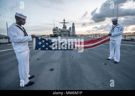 170911-N-UX013-804 NAVAL BASE GUAM (Sept. 11, 2017) Seaman Nayyaamunhotep Stubbs from West Palm Beach, Fla., left, and Hospitalman Kane Peters from St. Louis, fold the ensign during evening colors detail on the flight deck of the amphibious dock landing ship USS Ashland (LSD 48). Ashland flew the ensign at half-mast in honor of 9/11 victims during a scheduled port visit in Guam. (U.S. Navy photo by Mass Communication Specialist 3rd Class Jonathan Clay/Released) Stock Photo