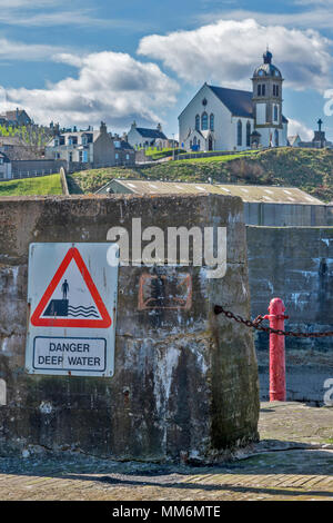 MACDUFF ABERDEENSHIRE SCOTLAND SHIPYARD OR BOATYARD DANGER DEEP WATER SIGN AND PARISH CHURCH ON HILL Stock Photo