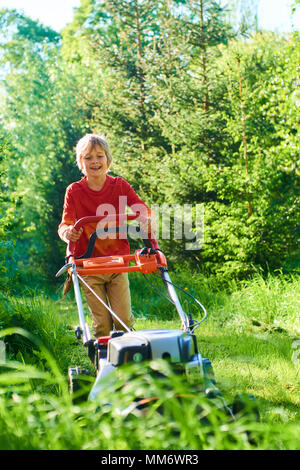 Child boy helping in the garden mowing lawn  with a lawn mower Stock Photo