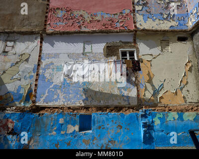 Wall of the old house, decorated in multicolored squares of blue, white, pink and brown colors, a white wooden window, linen on the rope, a bright pic Stock Photo