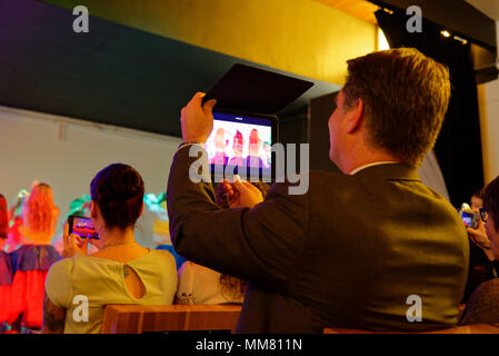 A man in a suit filming a school show with an ipad Stock Photo
