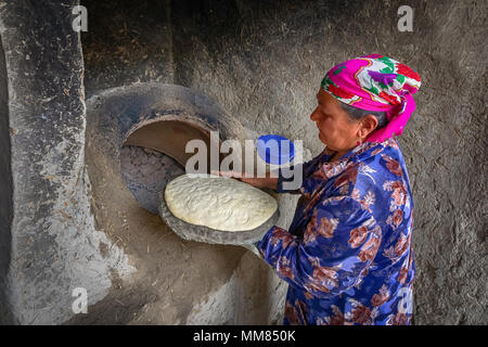 Bukhara, Uzbekistan - April 20 2018: An elderly woman is preparing to put the flatbread in to the tandoor - a traditional Uzbek oven Stock Photo