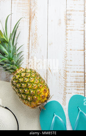 Flat Lay Arrangement Composition with Tropical Fruits Pineapple Women Hat Blue Slippers on White Planked Wood Background. Vacation Traveling Relaxatio Stock Photo