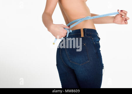 Young woman measuring waist with a tape. Fit and healthy girl with blue jeans on white background. Stock Photo