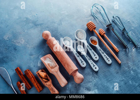 Cooking tools and ingredients flat lay with copy space. Baking header with measuring  spoons, wooden scoops, whisks, rolling pin, cookie cutters, sugar, flour,  eggs and cinnamon on a blue background. Stock Photo