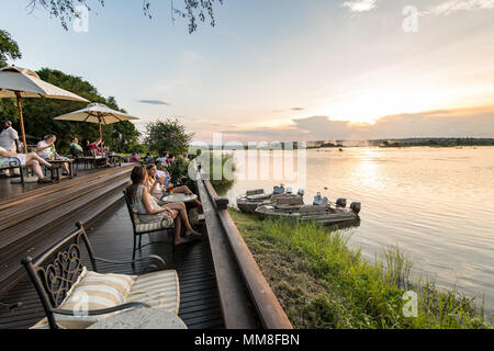 A group of hotel guests of the Royal Livingstone Hotel sit on the sundeck and watch the sun set over the Zambezi River Livingstone, Zambia Stock Photo