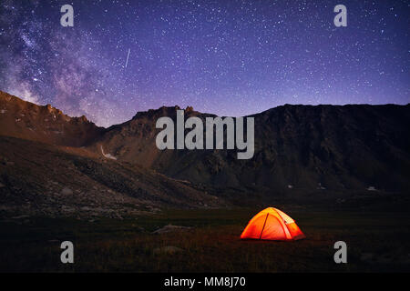 Orange tent glows under night sky full of stars and Milky way in the mountains in Kazakhstan Stock Photo