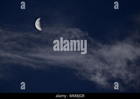 Crescent moon behind high altitude cirrus clouds against a blue sky Stock Photo