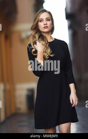 https://l450v.alamy.com/450v/mm8jm9/blonde-woman-in-urban-background-beautiful-young-girl-wearing-black-elegant-dress-standing-in-the-street-pretty-russian-female-with-long-wavy-hair-h-mm8jm9.jpg