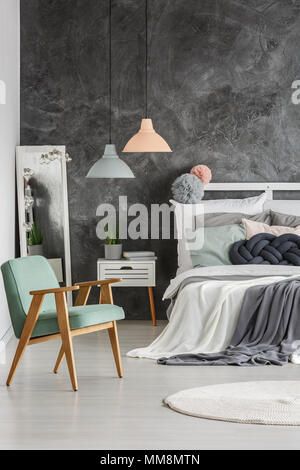 Stylish gray wall in a room with wooden bed and armchair Stock Photo