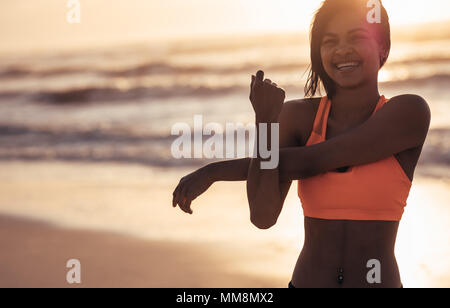Smiling woman stretching arms at the sea shore. Female athlete doing warm up workout at the beach. Stock Photo