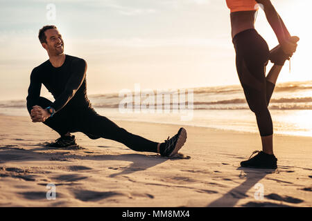 Young people exercising on the beach in morning. Runner stretching and warming up along the sea shore and having a chat.