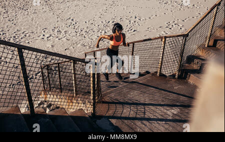 Athletic woman runs up the steps on the beach. Athlete in sportswear training on concrete steps.