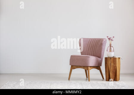 Cute pink flowers in glass vase placed on wooden table standing by small chair Stock Photo