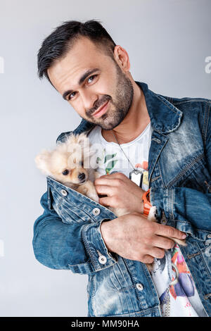 man in denim jacket holds pomeranian dog. Stock Photo