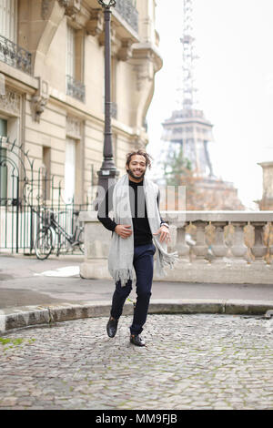 Afro american boy running with Eiffel Tower in background, wearing grey scarf and black sweater. Stock Photo