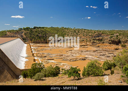 Burdekin Falls dam with high spillway overflowing and coffee coloured water flowing into rocky river bordered by wooded hills under blue sky, Qld Aust Stock Photo