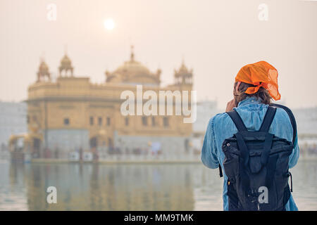 A tourist with an orange bandana is taking a picture at the beautiful Golden Temple of Amritsar, Punjab, India. Stock Photo