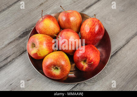 Metal bowl full of red ripe apples placed on gray wooden desk. Stock Photo