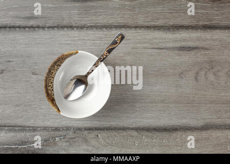 Table top view on small empty porcelain bowl with silver decorated spoon, placed on gray wood desk. Stock Photo