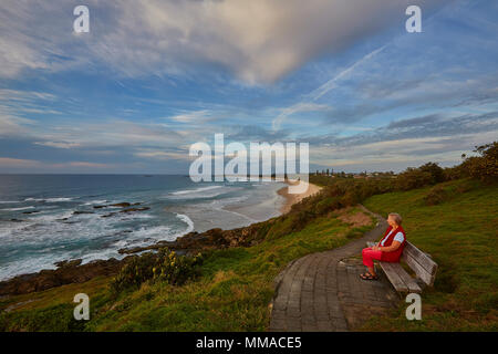 A woman on her own sat on a bench at Boambee headland looking at Murray's Beach, New South Wales, NSW, Australia Stock Photo