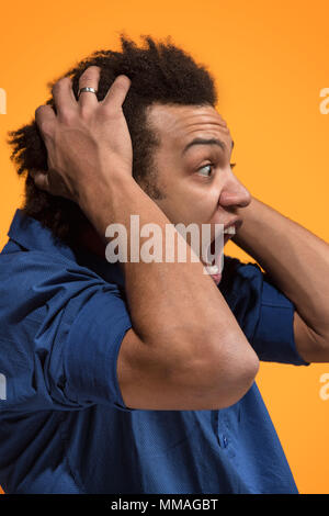 The young emotional angry man screaming on orange studio background Stock Photo