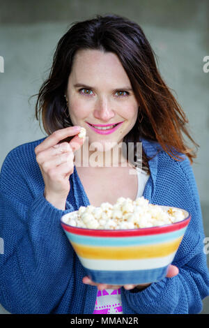young brunette woman eating popcorn from a bowl and looking at camera Stock Photo