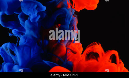 Red and blue ink in water shooting with high speed camera. Bloody paint dropped, reacting, creating abstract cloud formations and metamorphosis on bla Stock Photo