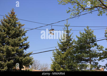 Pair of black Nike gymshoes hanging from electrical wires spanning overhead over a street, usually a sign of a drug house nearby. Stock Photo