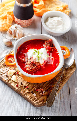 Borsch traditional Ukrainian and Russian soup with meat, beets and cabbage. Meat soup in an orange bowl on a light wooden background. Stock Photo