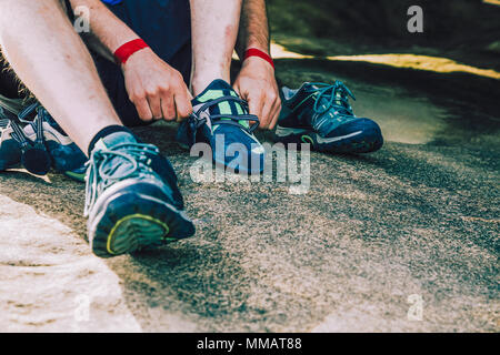 Close up of rock climber man with wristbands putting climbing shoes on sitting on a rock Stock Photo