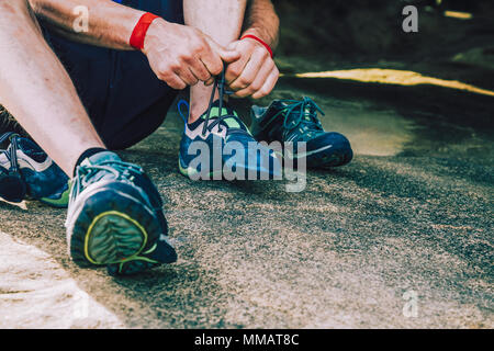 Close up of rock climber man with wristbands putting climbing shoes on sitting on a rock Stock Photo