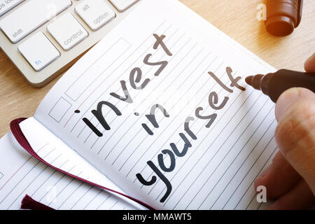 Man is writing invest in yourself in a note. Stock Photo