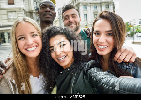 Multiracial group of friends taking selfie in a urban street with a muslim woman in foreground. Three young women and two men wearing casual clothes. Stock Photo