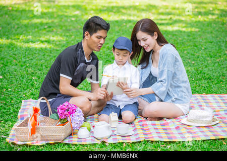 Parents as Teachers concept: Teen family with one kid happy education moment in the park. Stock Photo