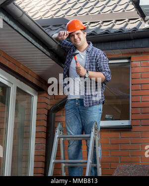 Portrait of smiling carpenter in hardhat standing on top of stepladder Stock Photo