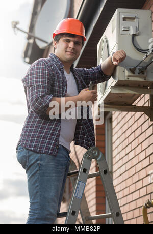Portrait of smiling male repairman repairing air conditioner system Stock Photo