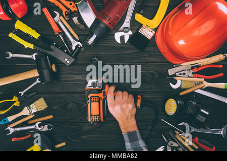 cropped shot of worker holding electric screwdriver and various supplies on wooden tabletop Stock Photo