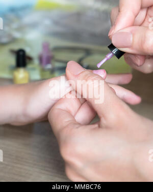 Mom applying nail polish to her daughter. Fun activity at home or girl birthday party. Stock Photo