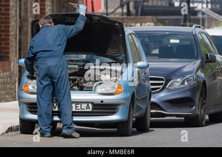 Car mechanic wearing overalls working on a car with the bonnet up in the UK.