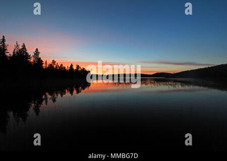 Beautiful and colorful sunset with the reflection of the forest in the Skarvsjon lake, Lapland, Sweden, Europe Stock Photo